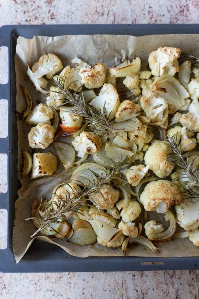 Baked cauliflower, onion, garlic, rosemary on a tray with olive oil, salt and pepper
