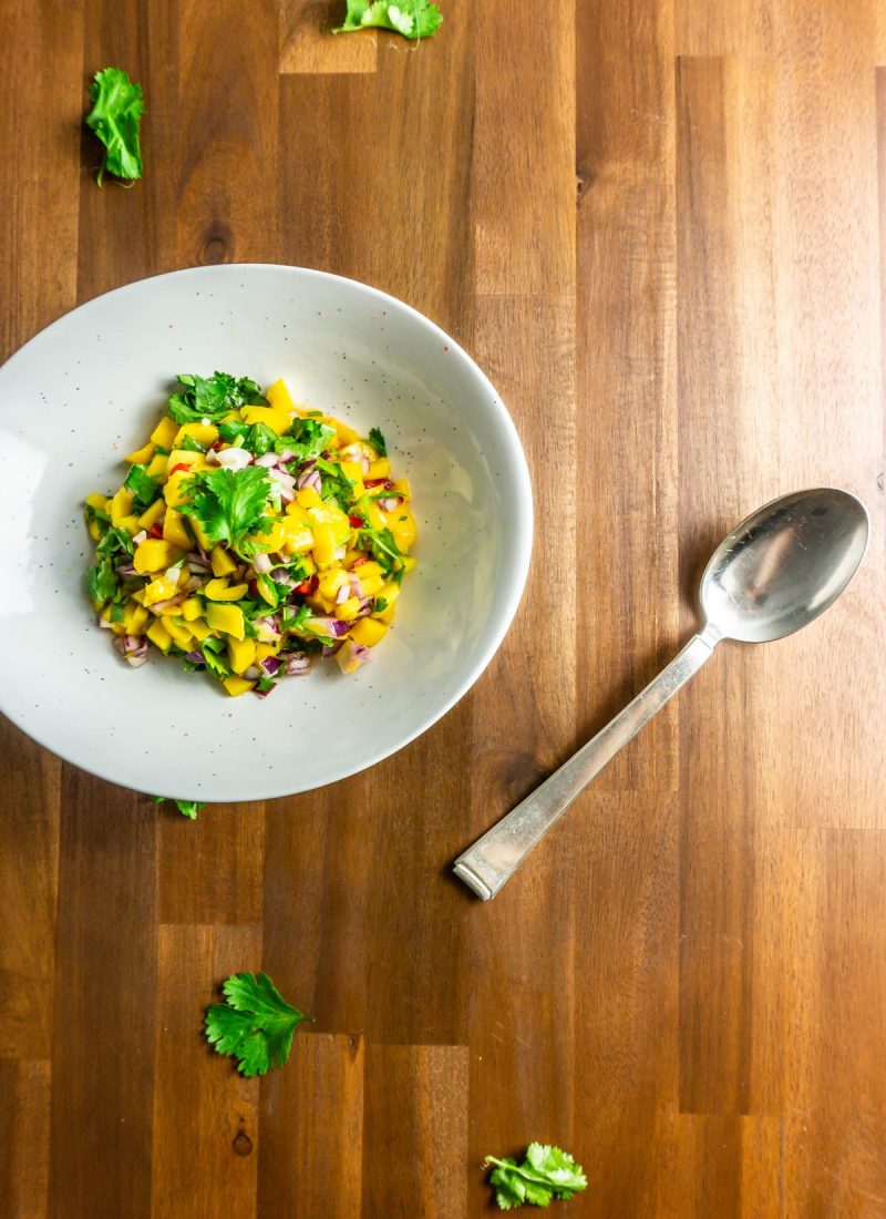 Mango Salsa in a white bowl on a wooden background with a spoon