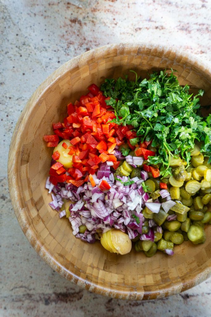 Cut potatoes with cut gherkins, onions, red peppers, and parsley cut in a bowl