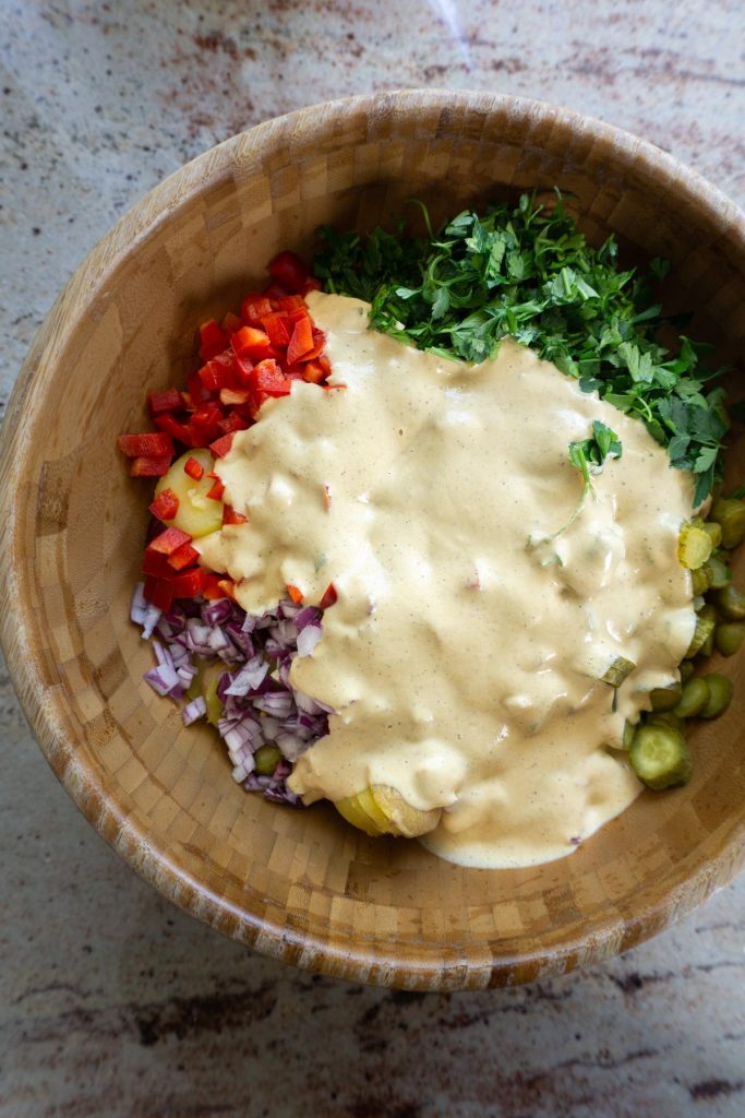 Cut potatoes with cut gherkins, onions, red peppers, and parsley cut in a bowl with added sauce