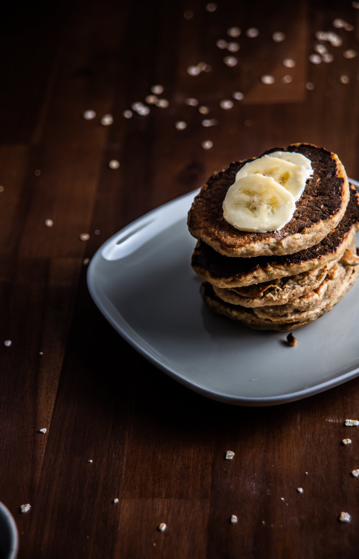 Stacked Easy Pantry Staple Pancakes with sliced bananas on top and strewn oats in the background