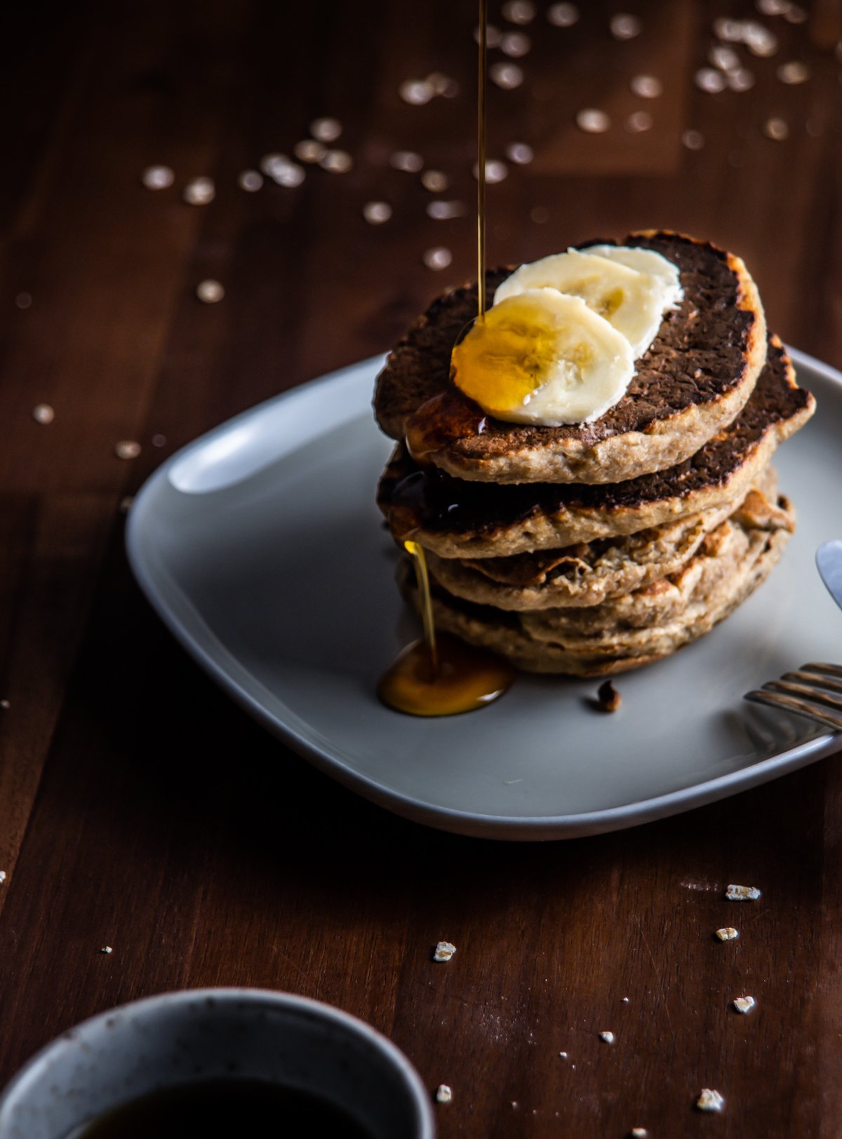 Stacked Easy Pantry Staple Pancakes with sliced bananas on top with maple syrup running on the pancakes