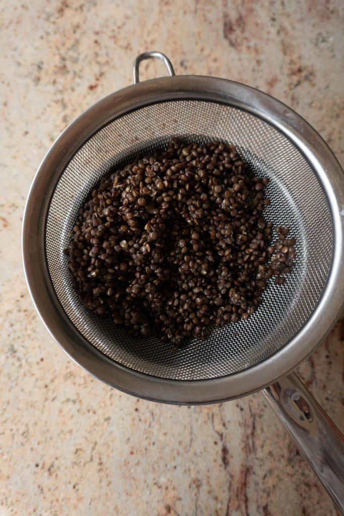 Cooked beluga lentils draining in a sieve