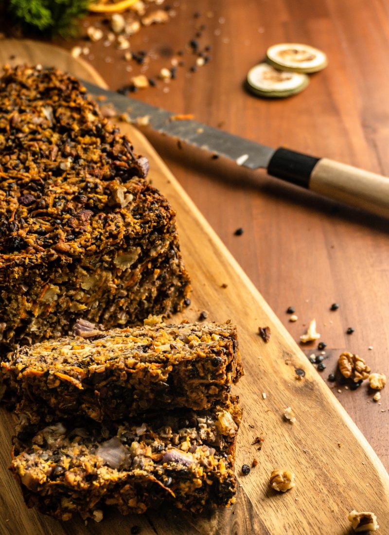 Lentil Mushroom Walnut "Meat" Loaf cut into pieces on a chopping board with a knife in the background. Shot from above.