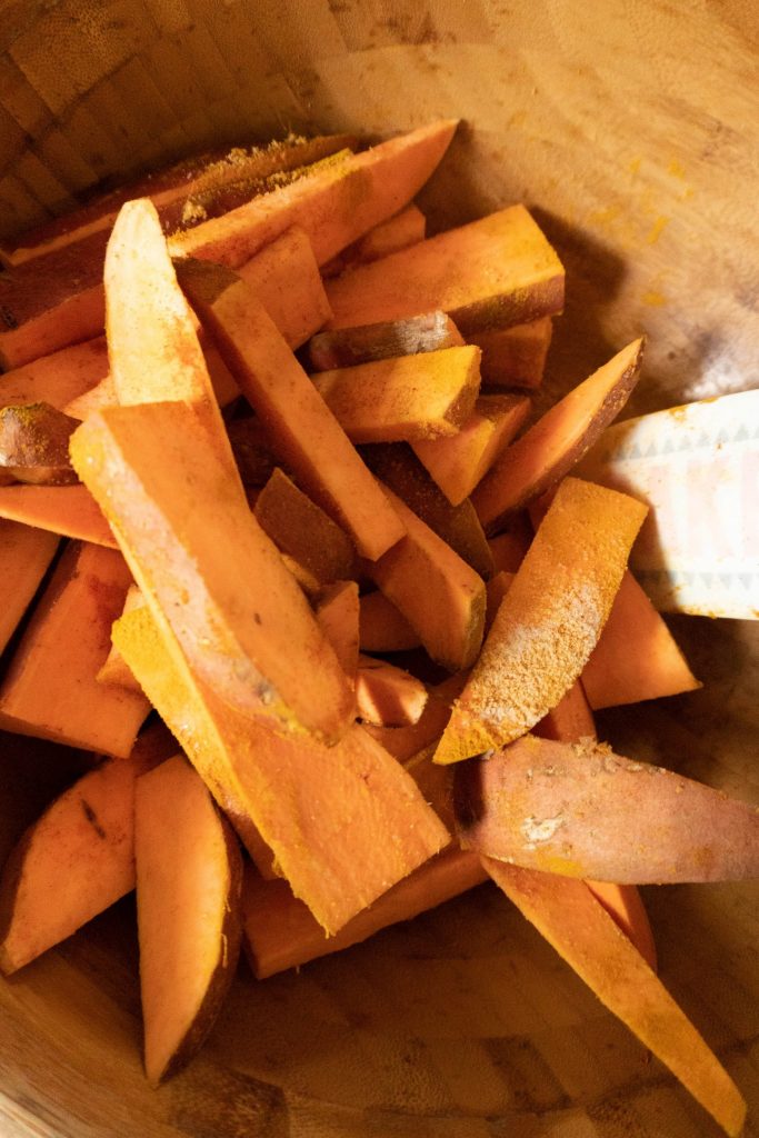 Sweet potatoes cut into wedges being covered in a bowl with spices