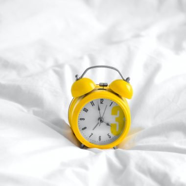 Yellow alarm clock on white sheets