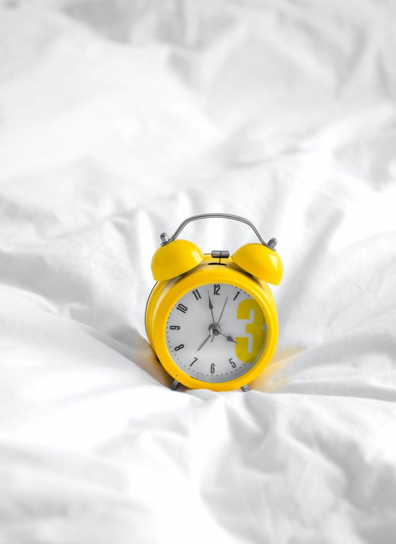 Yellow alarm clock on white sheets