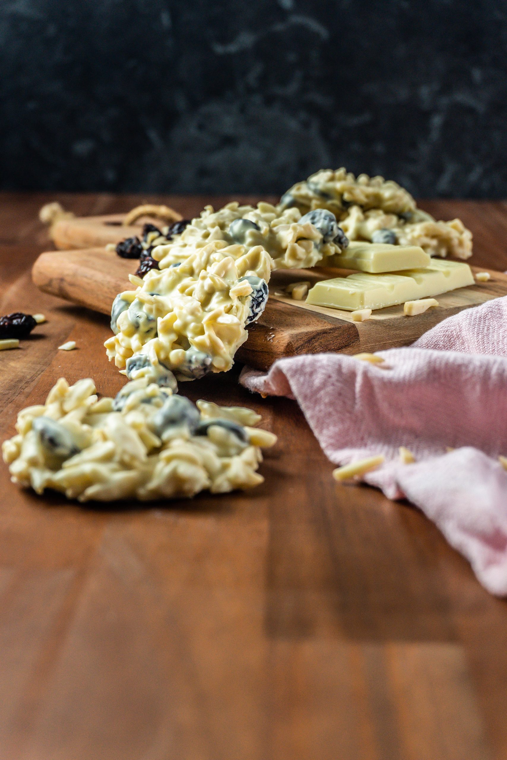 Shaved Almond and Cranberry White Chocolate Cookie in focus with more cookies scattered in the background Shaved Almond and Cranberry White Chocolate Cookie in focus with more cookies scattered in the background and in the front