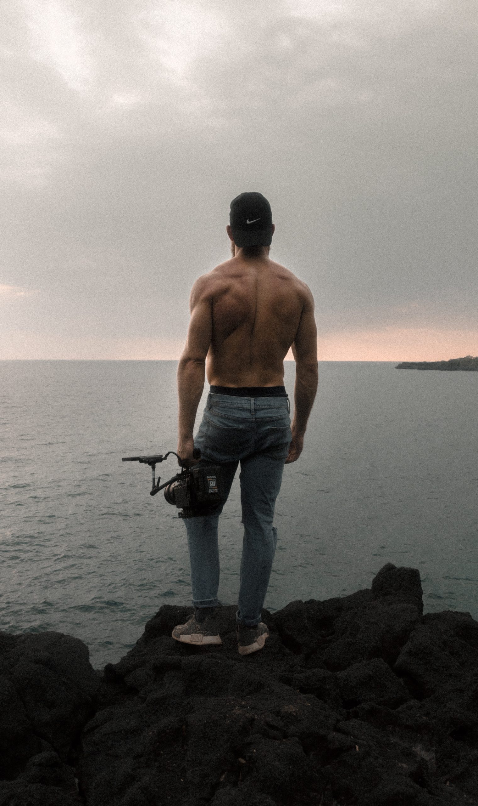 A man standing on a lake with a camera in hand and displaying back muscles