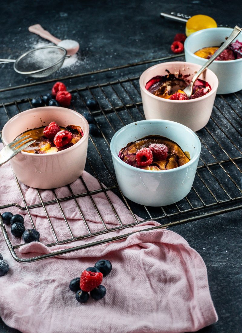 Five Minute Mini Cheesecakes on a baking tray surrounded with raspberries and blueberries covered with some powdered sugar and forks tugged into two mugs