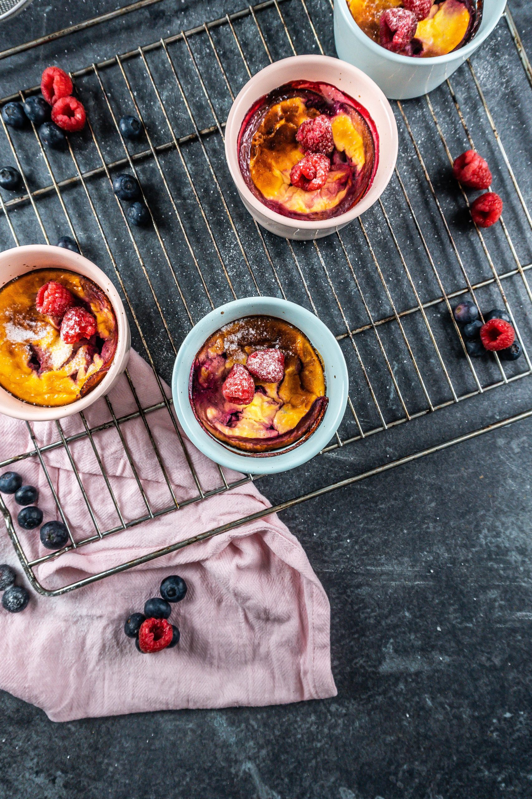 Five Minute Mini Cheesecakes on a baking tray surrounded with raspberries and blueberries covered with some powdered sugar