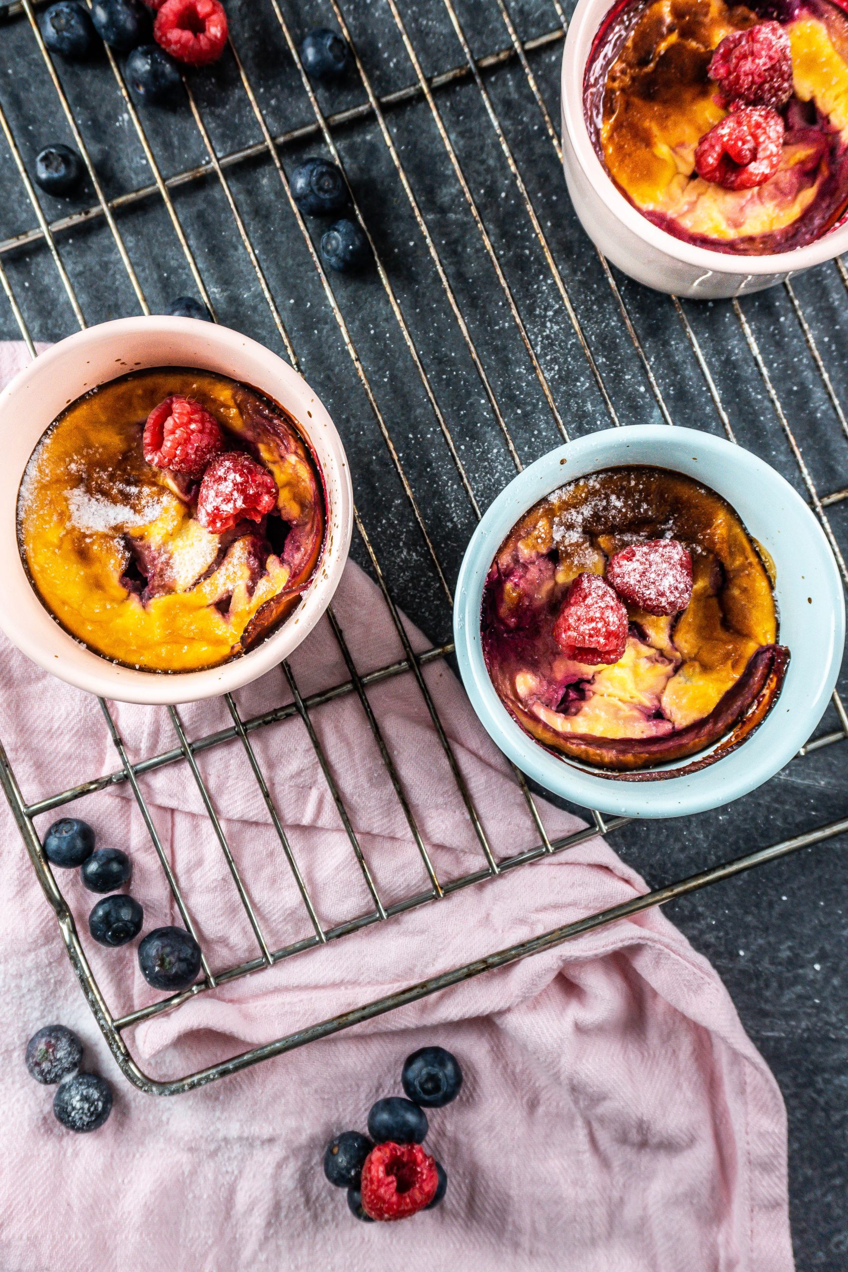 Five Minute Mini Cheesecakes on a baking tray surrounded with raspberries and blueberries covered with some powdered sugar; photographed from above