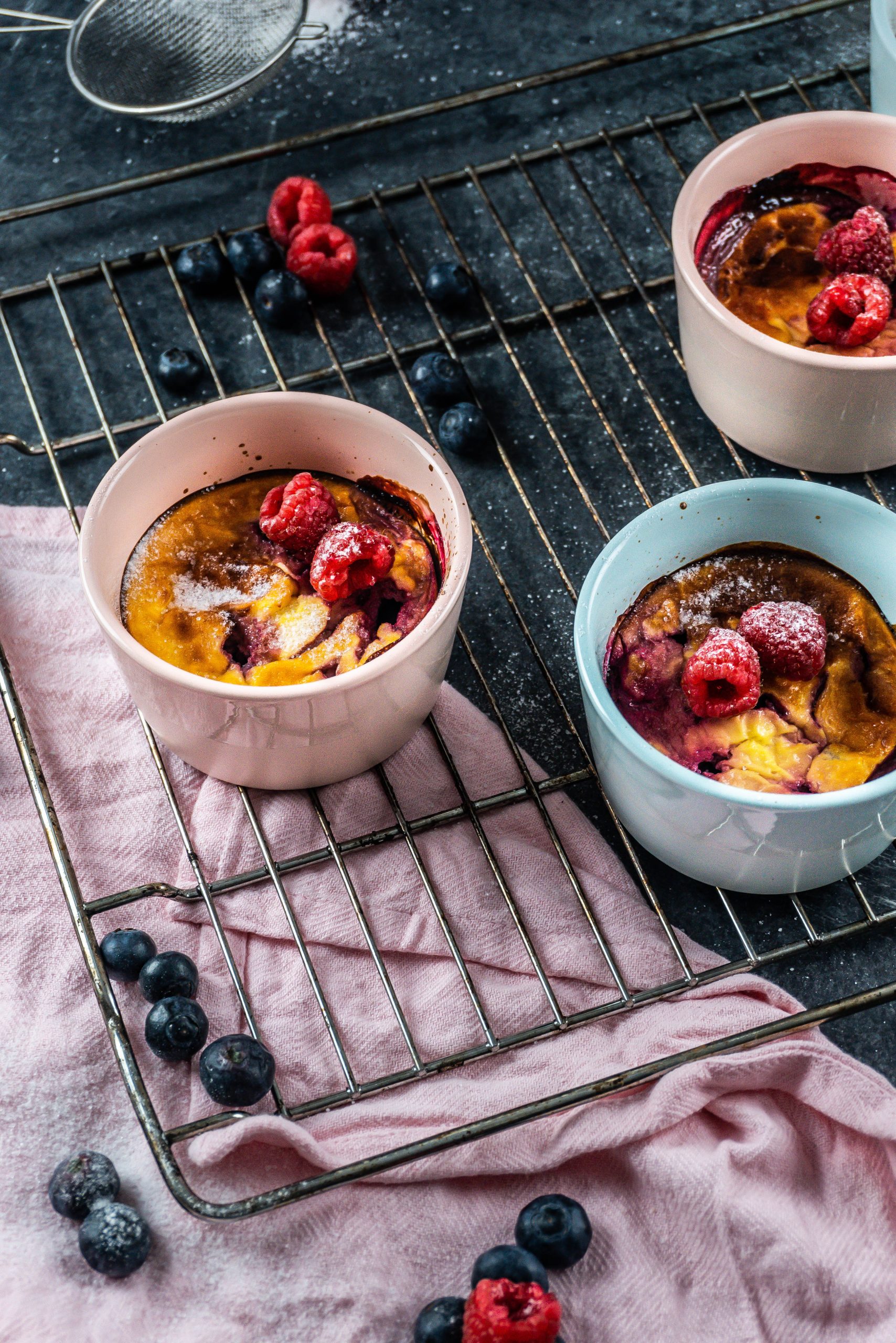 Five Minute Mini Cheesecakes on a baking tray surrounded with raspberries and blueberries covered with some powdered sugar