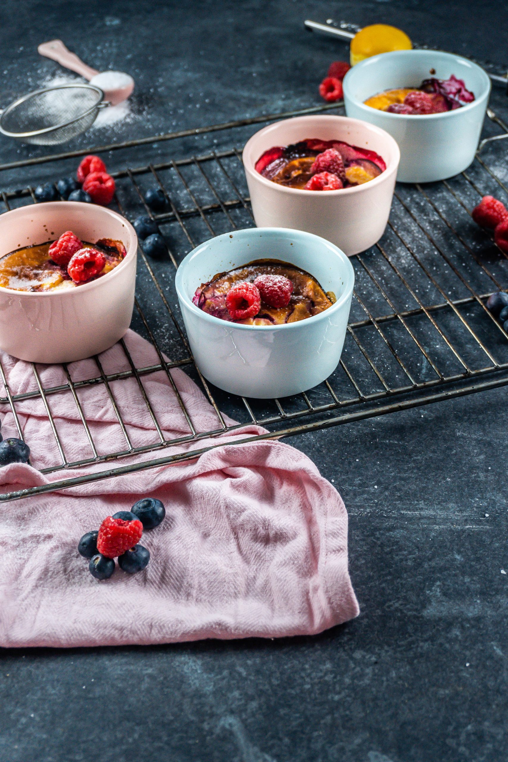 Five Minute Mini Cheesecakes on a baking tray surrounded with raspberries and blueberries covered with some powdered sugar