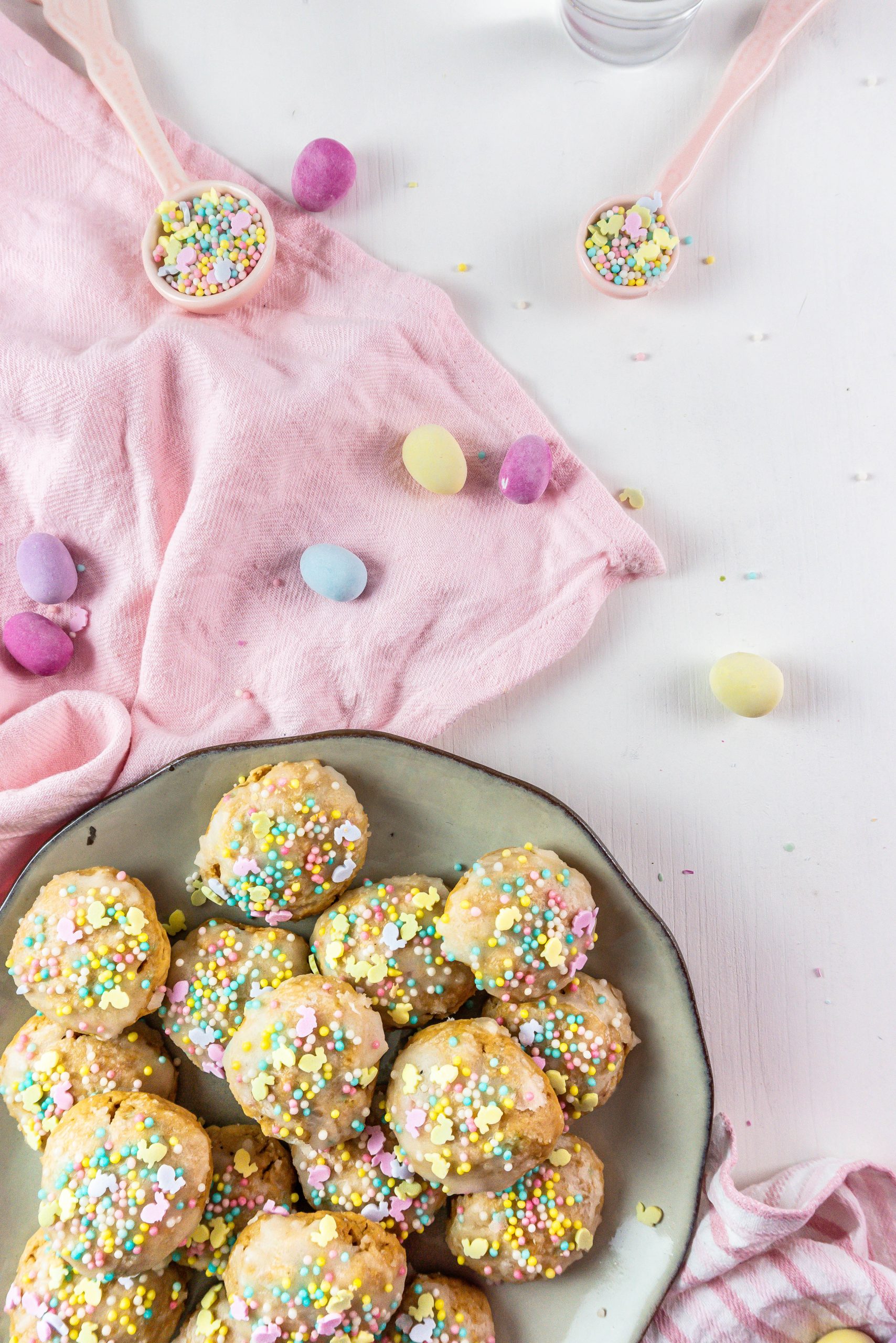 Italian Easter Cookies on a plate, surrounded by sprinkles, pastel Easter eggs and some dish towels