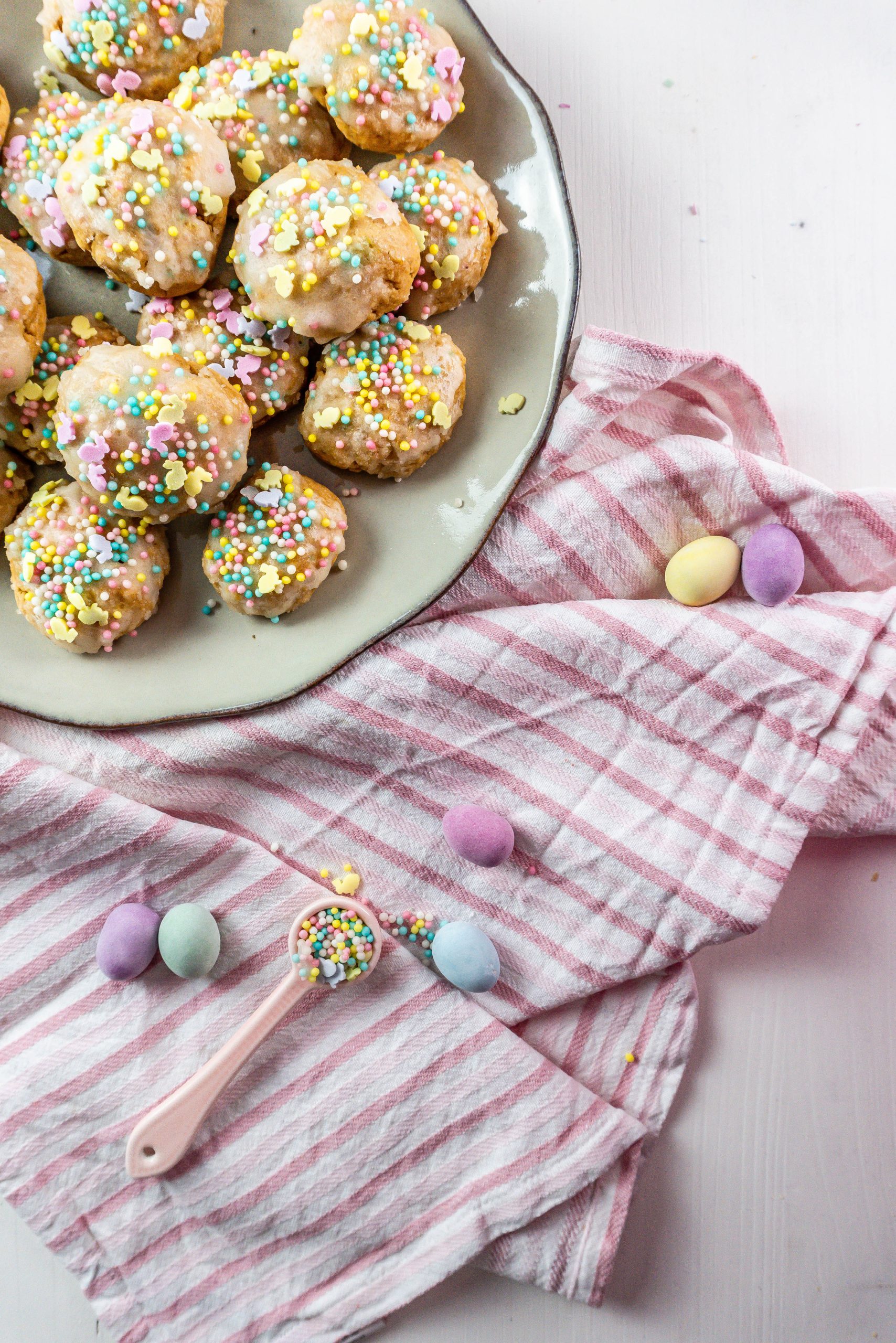 Italian Easter Cookies on a plate, surrounded by sprinkles, pastel Easter eggs and some dish towels; photographed from above