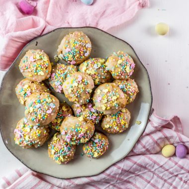 Italian Easter Cookies on a plate, surrounded by sprinkles, pastel Easter eggs and some dish towels