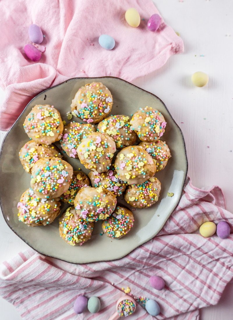 Italian Easter Cookies on a plate, surrounded by sprinkles, pastel Easter eggs and some dish towels