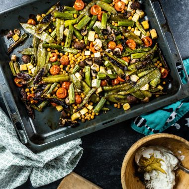 Spring Greens Oven Tray Bake with roasted garlic and sauce ingredients on the side; photographed from above
