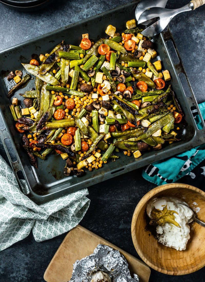 Spring Greens Oven Tray Bake with roasted garlic and sauce ingredients on the side; photographed from above