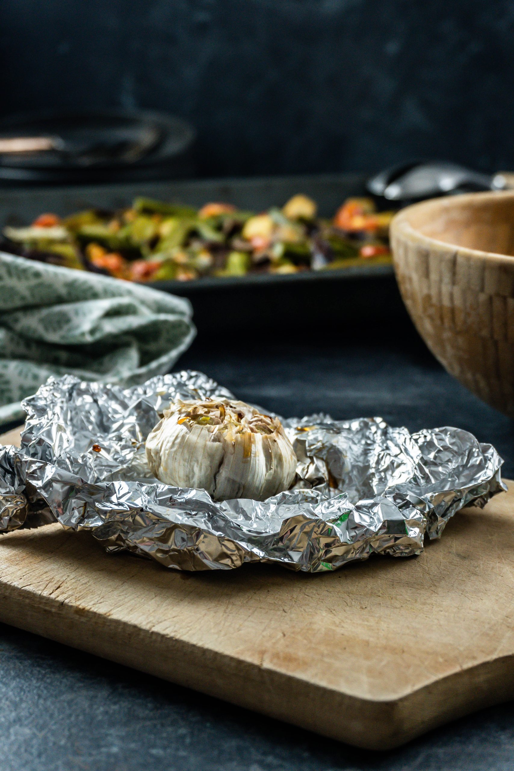 Roasted garlic wrapped in tin foil on a small wooden board