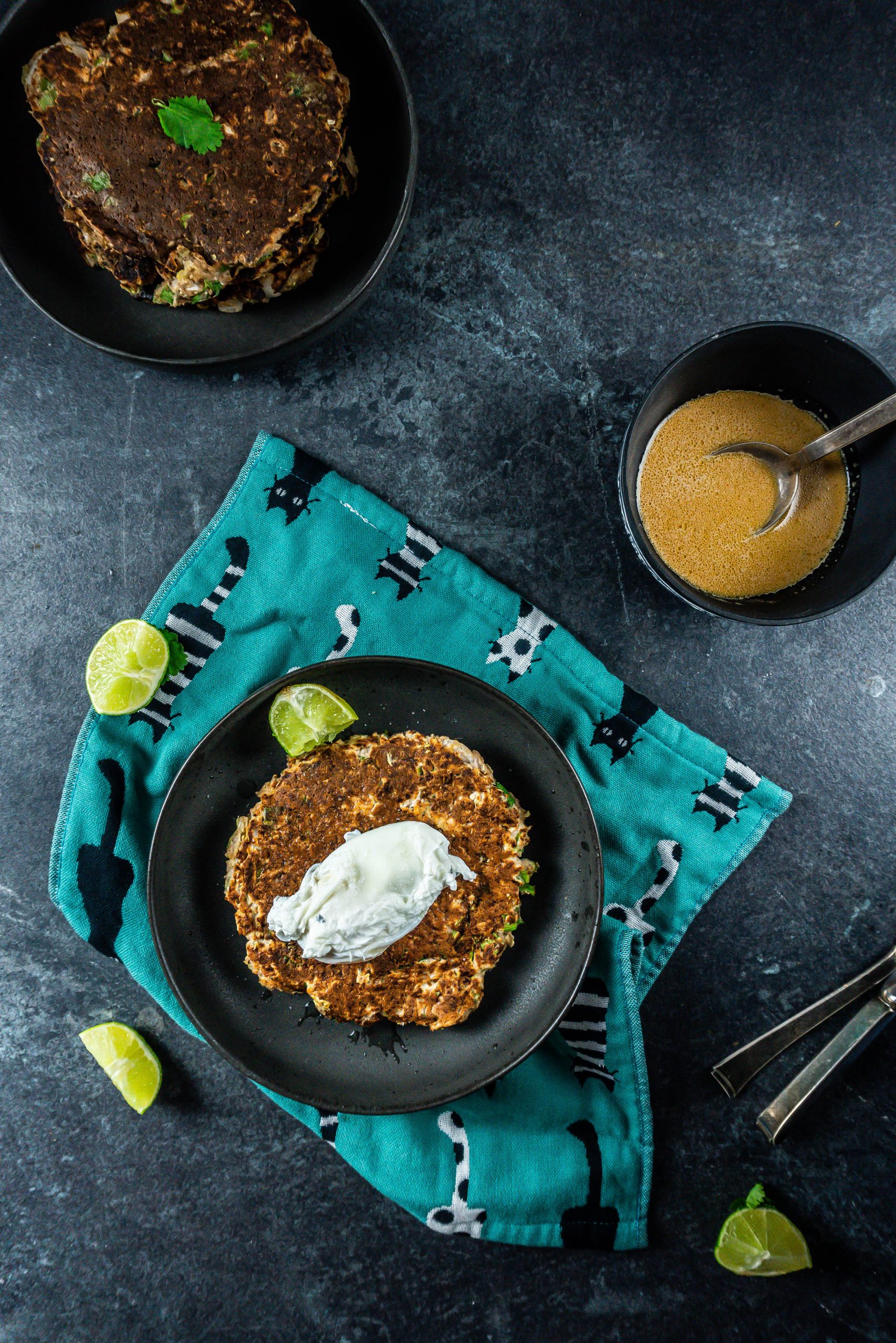 Cabbage pancakes on a plate with a poached egg on top and sauce at the side, photographed from above