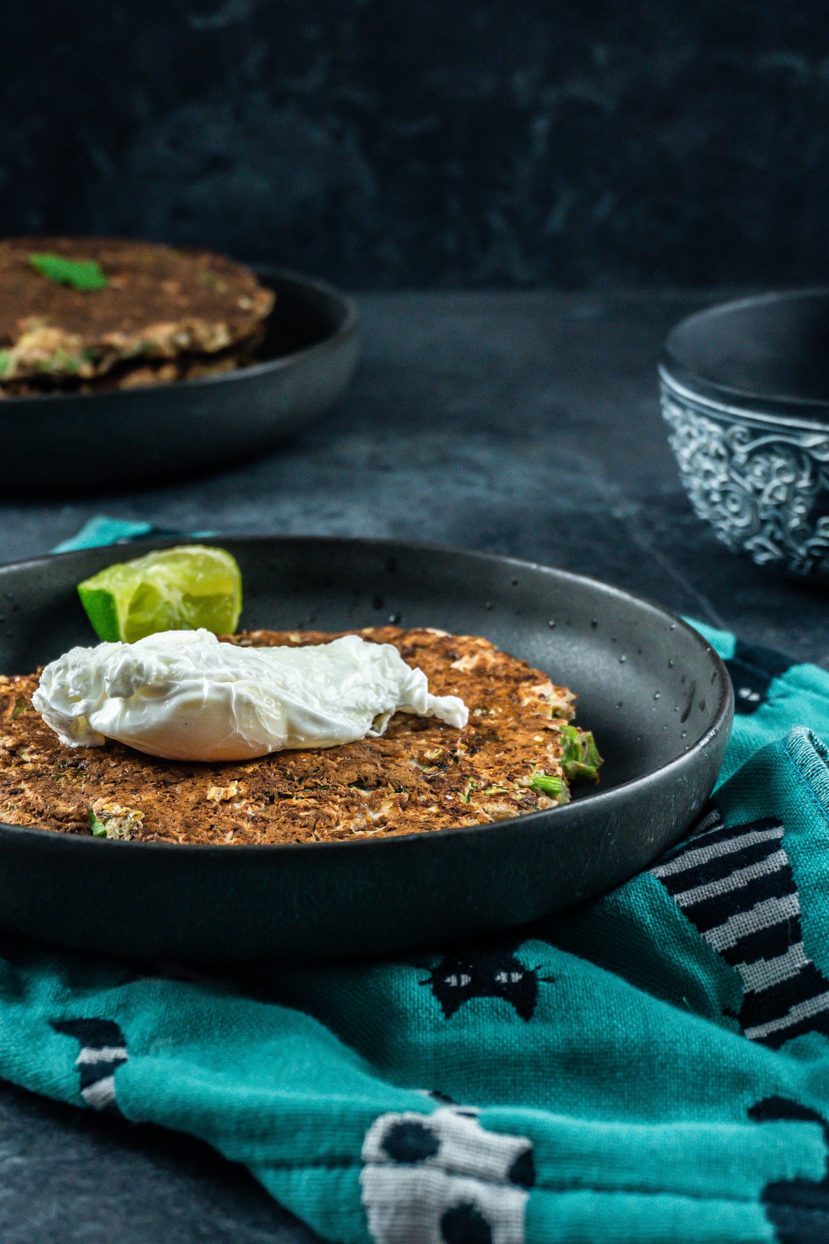 Cabbage pancakes on a plate with a poached egg on top and sauce at the side, photographed from a side-angle