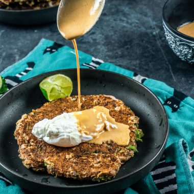 Peanut butter sauce being poured onto the cabbage pancakes with a poached egg
