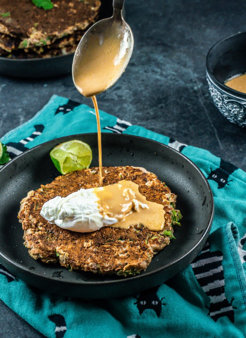 Peanut butter sauce being poured onto the cabbage pancakes with a poached egg