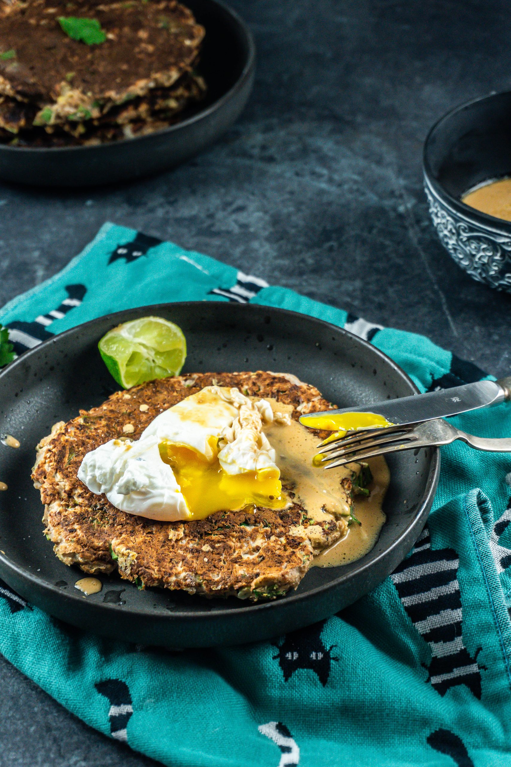 A knife and fork tugging to the cabbage pancake with poached eggs and peanut butter sauce
