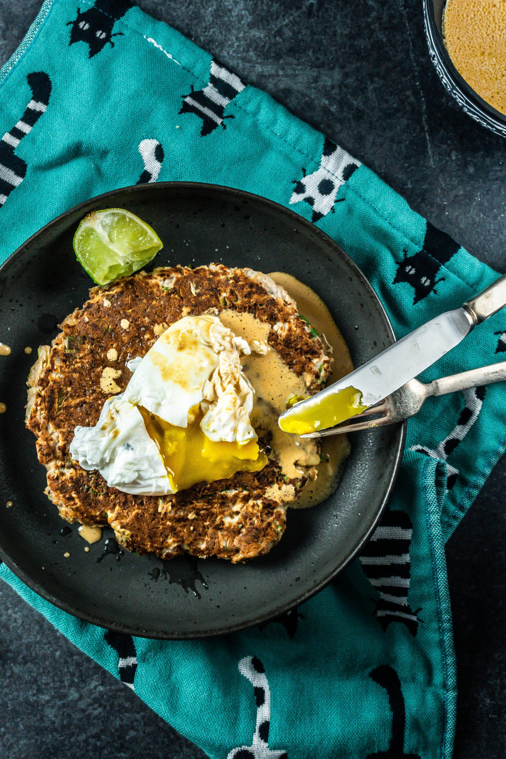 A knife and fork tugging to the cabbage pancake with poached eggs and peanut butter sauce