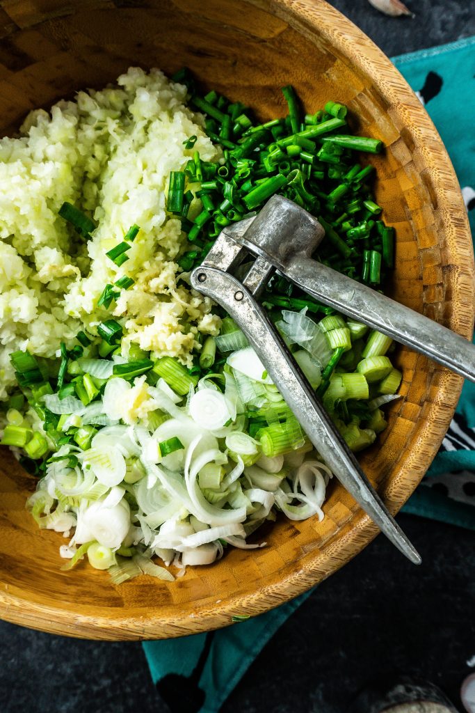 Cabbage, spring onions, chives, and crushed garlic in a bowl ready to be mixed