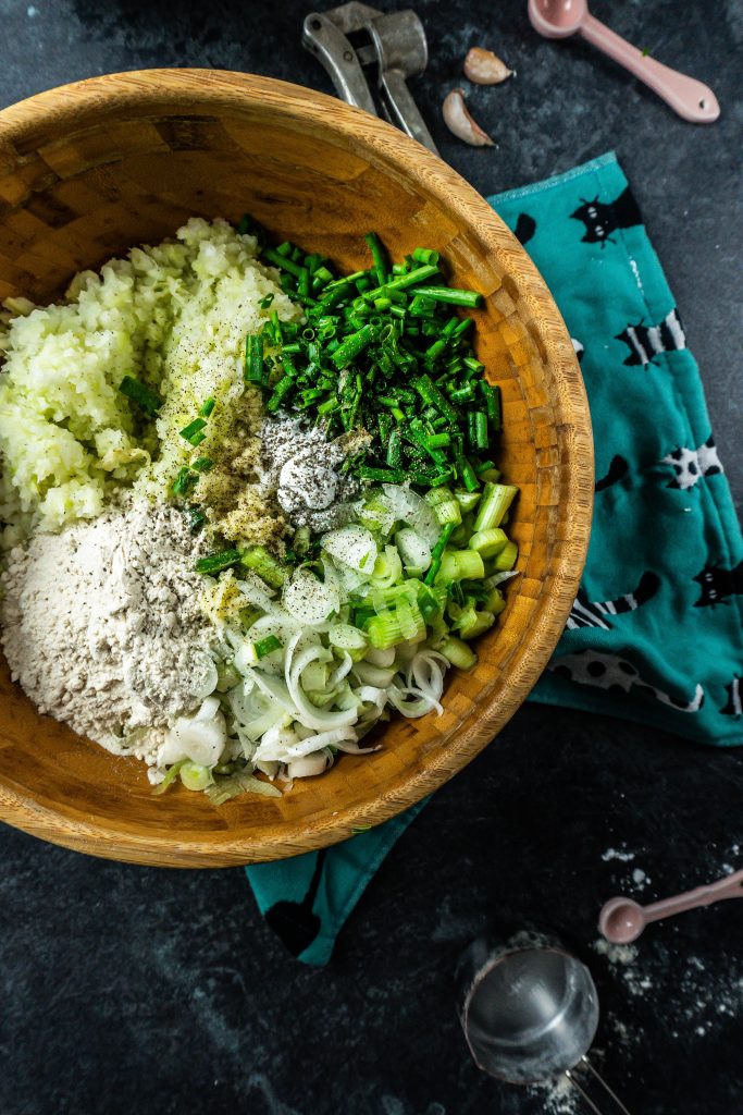 Cabbage, chives, spring onions, crushed garlic, gluten-free flour, and baking powder in a bowl ready to be mixed