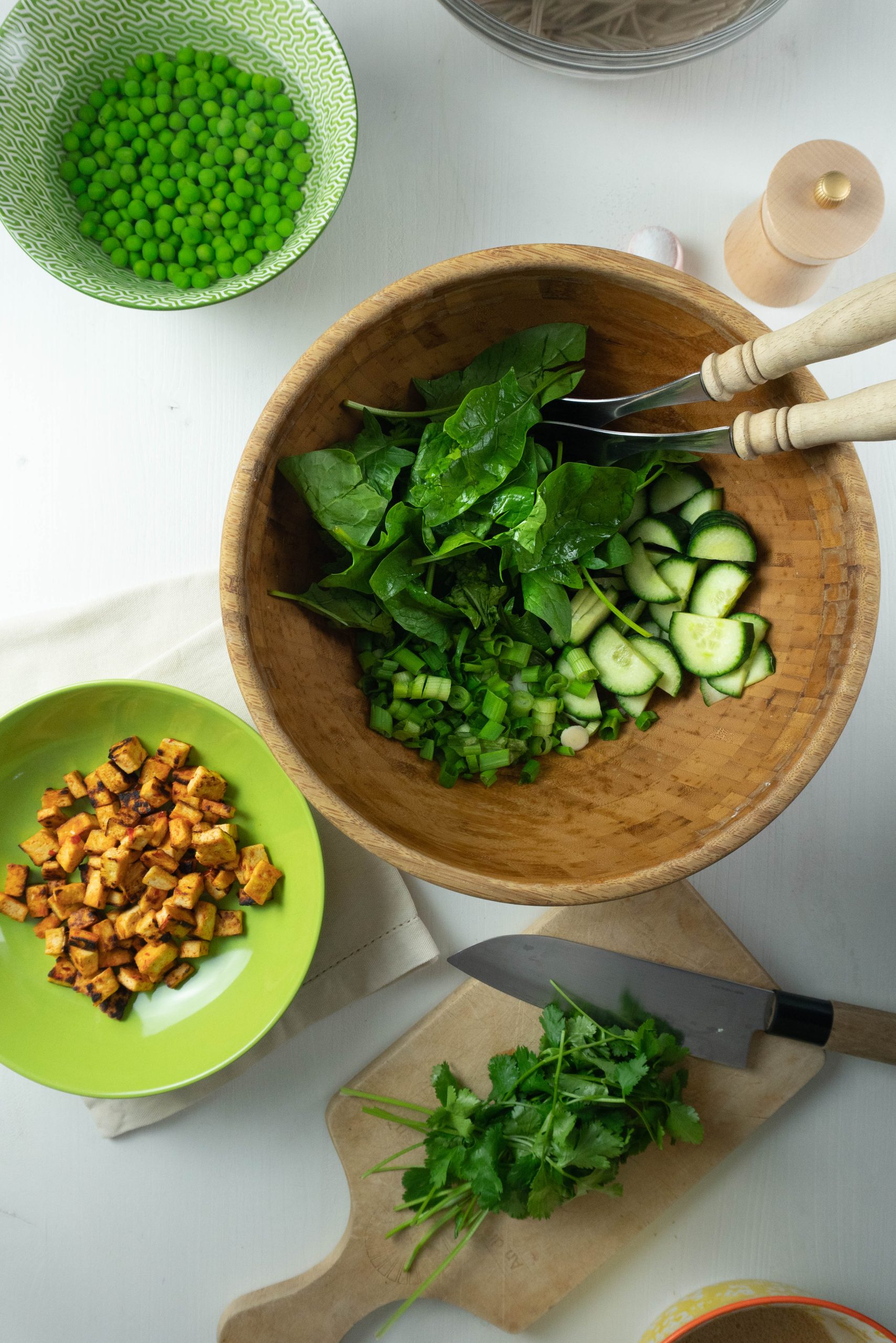 Peas, tofu, cilantro, spinach, cucumber, and spring onions are being prepared in a salad bowl