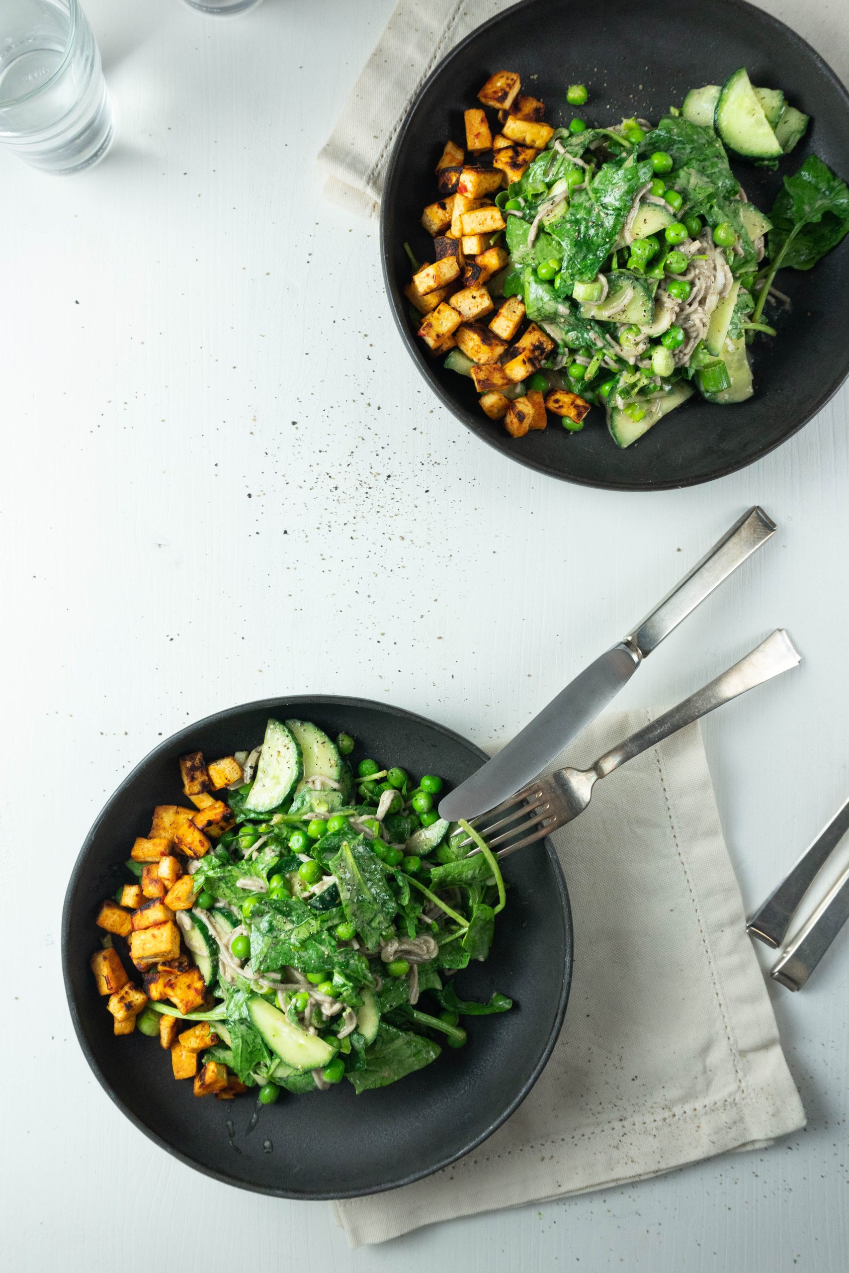 Perfect soba noodle salad with tofu on the side plated on two plates; photographed from above