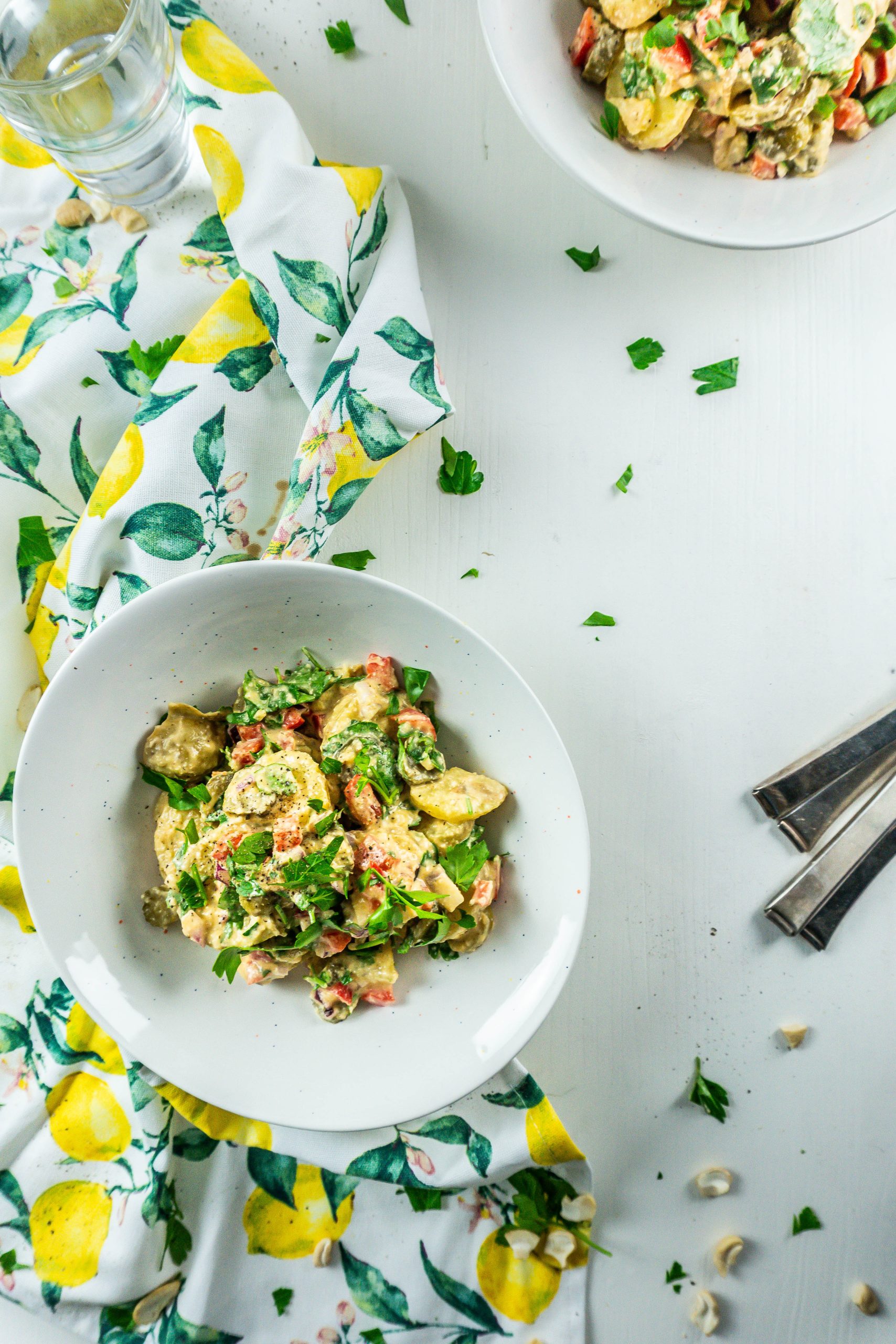 Vegan Potato Salad in two bowls, ready for serving with cutlery and water glasses at the side; photographed from above