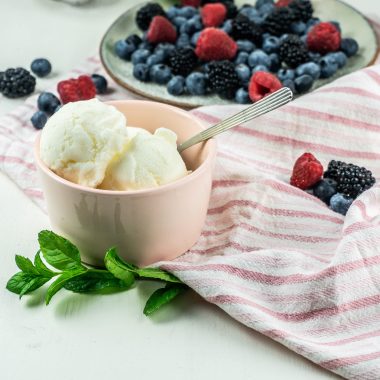 Cool and creamy yogurt ice cream scoops in a small bowl with a spoon stuck into it surrounded by berries
