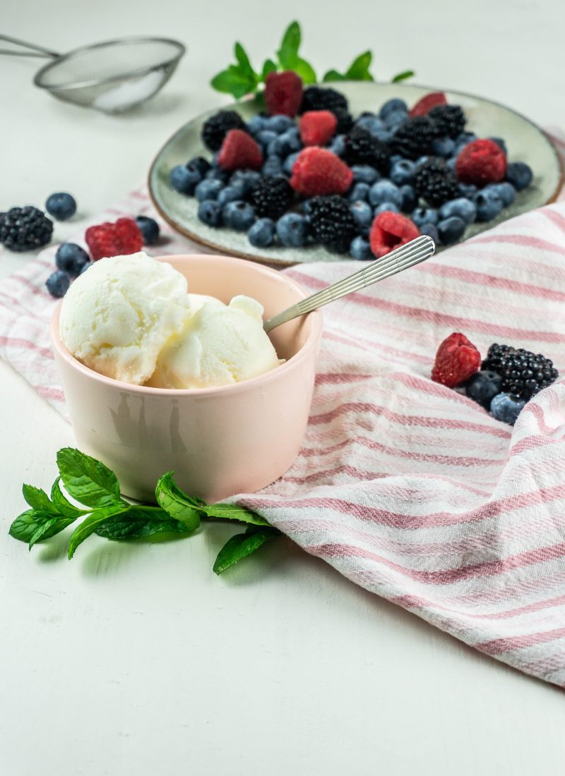 Cool and creamy yogurt ice cream scoops in a small bowl with a spoon stuck into it surrounded by berries