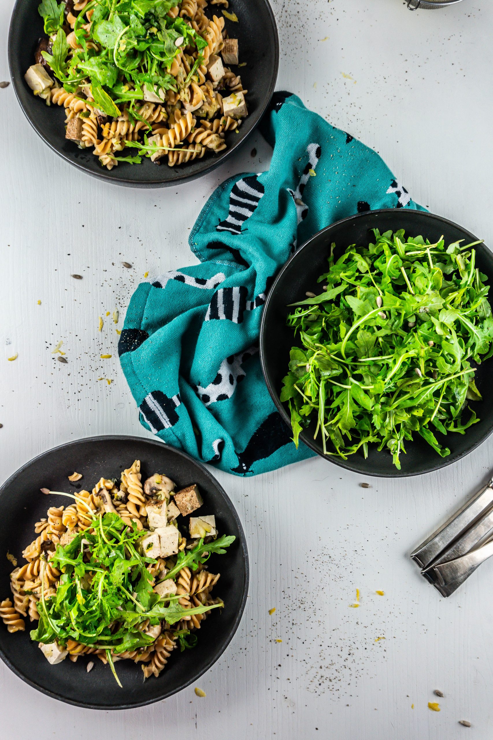 15-Minute Summer Pasta on a plate with lemon zest and arugula in the background and cutlery laying to the side; photographed from above