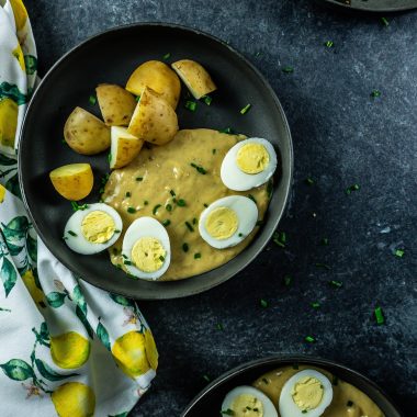 German eggs in mustard sauce with potatoes on a dark plate; photographed from above