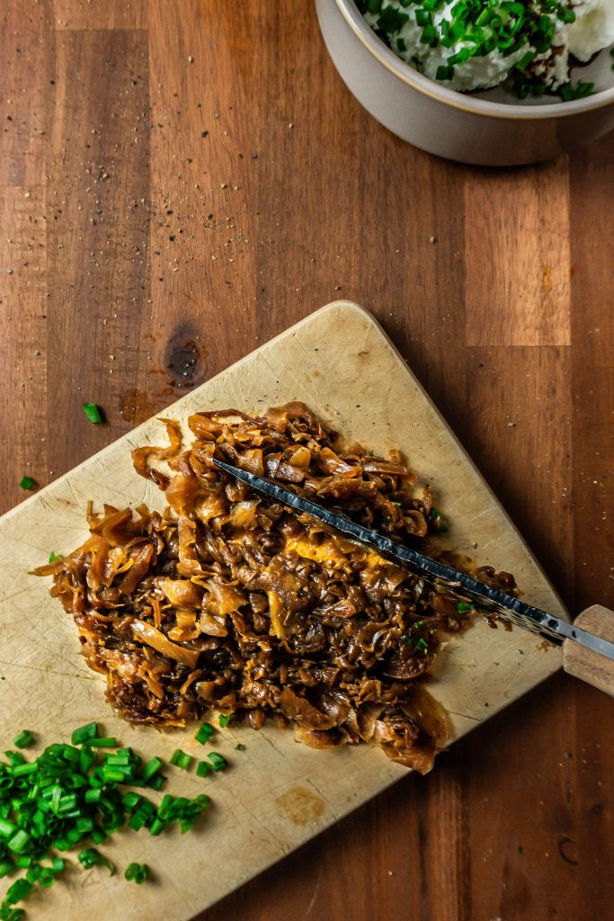 Caramelized onions being finely chopped on a small wooden board