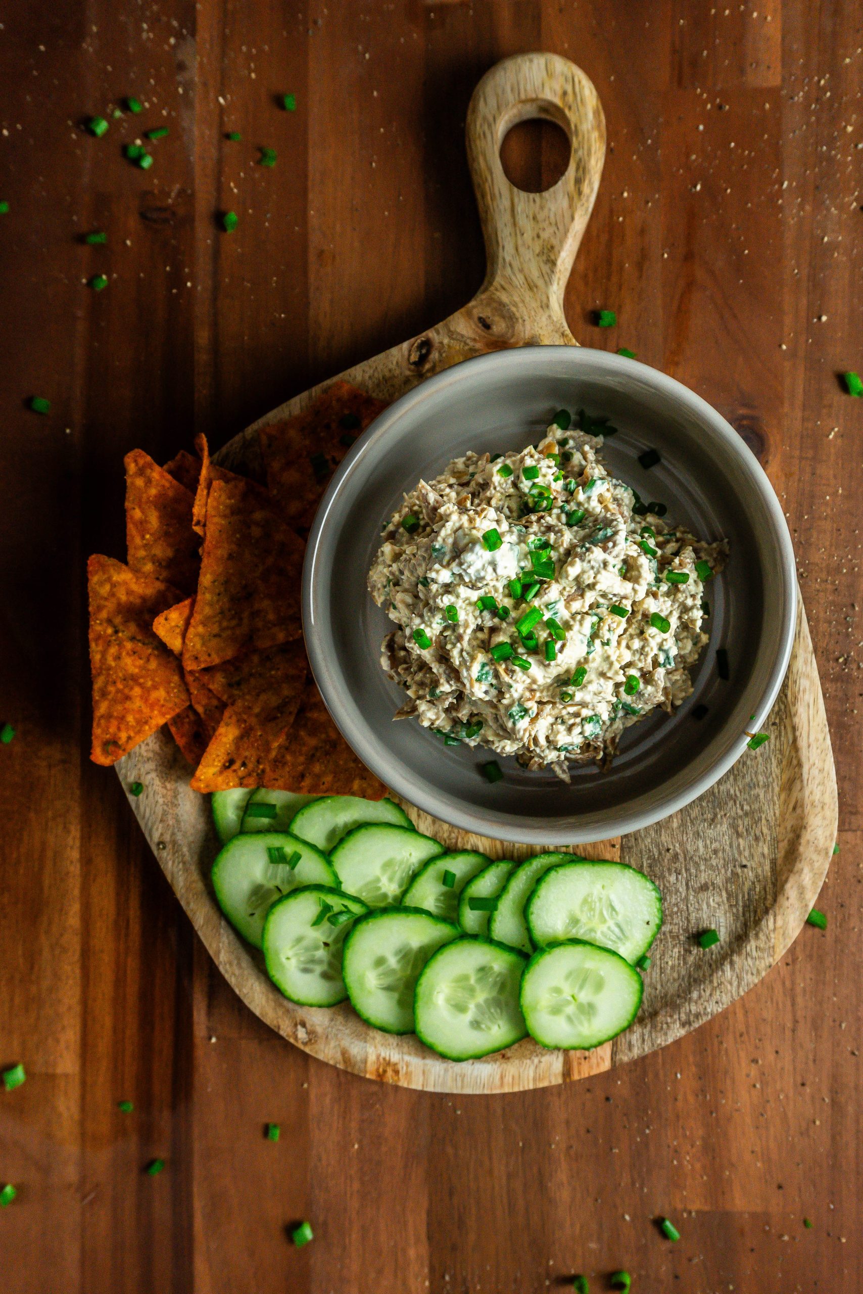 Caramelized onion dip with cucumbers and nachos laying on the side and chives strewn across