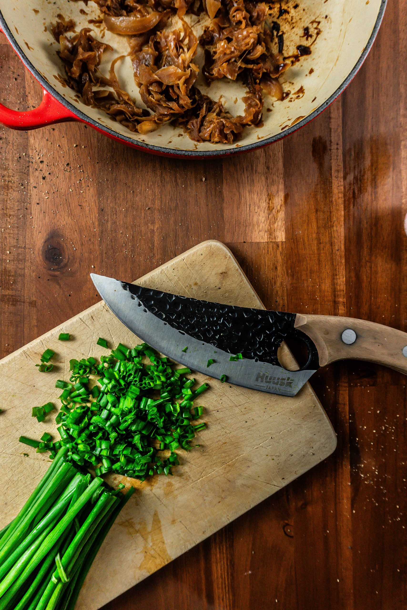 Chives being chopped on a small wooden board with caramelized onions visible in the background