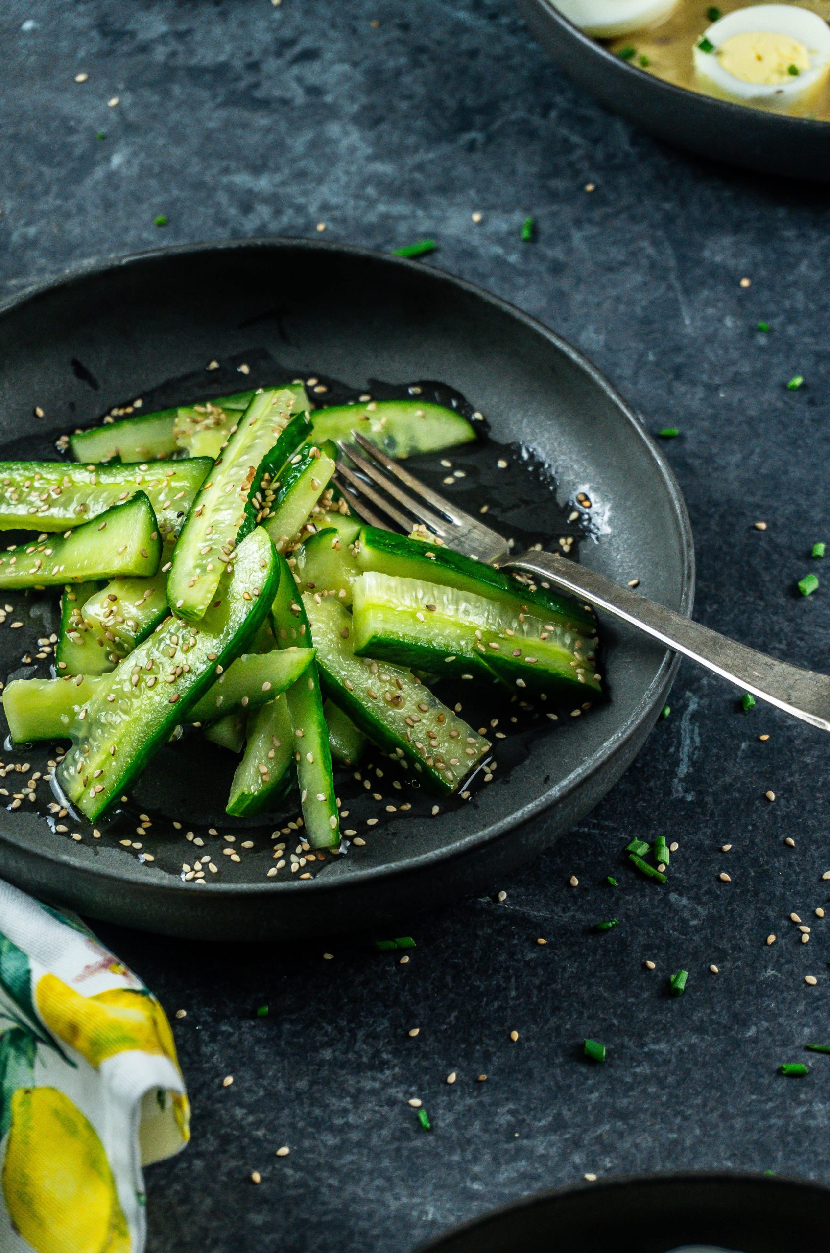 Japanese-Inspired Cucumber Salad with a fork on the plate and sesame seeds scattered in the background; photographed from a side-angle