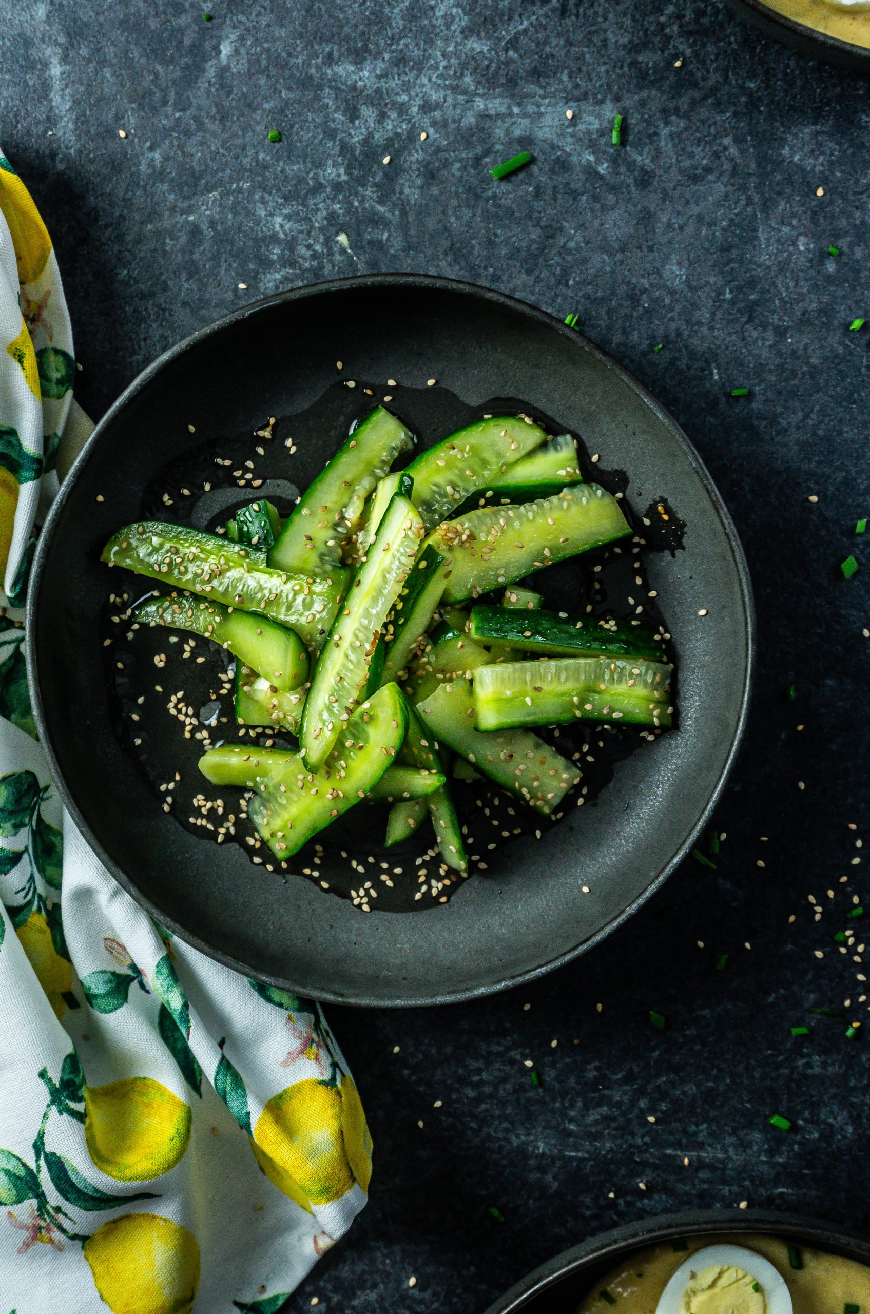Japanese-Inspired Cucumber Salad on a black plate with sesame seeds scattered in the background; photographed from above