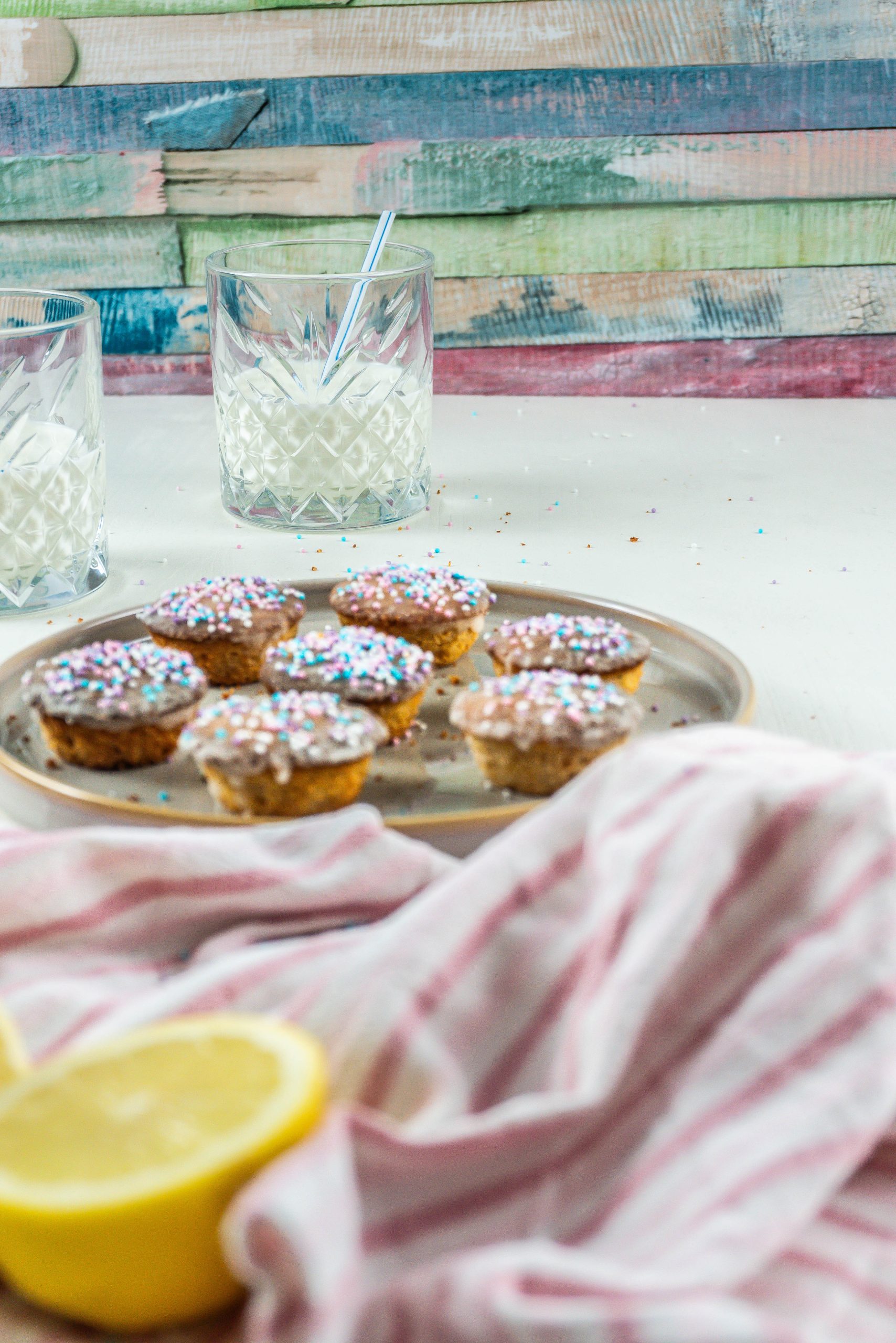 A glass of milk with a straw in focus with Lemon Mascarpone Mini Muffins visible in the front