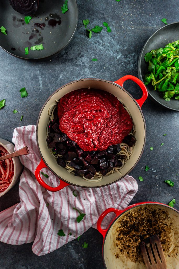 Gluten-free noodles, fried onions, cut up beets, and creamy blender beetroot pasta sauce ready to be mixed in a pot