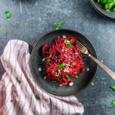 Creamy blender beetroot pasta with crumbled feta and chopped parsley; photographed from above with a fork laying on the plate