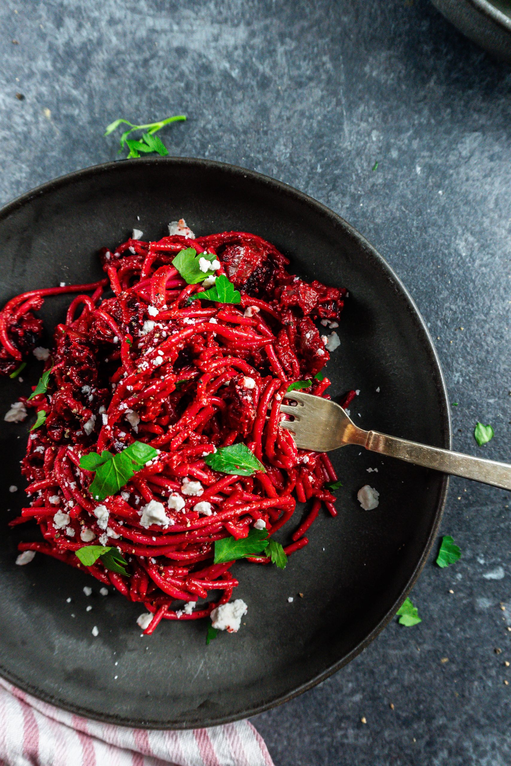 Creamy blender beetroot pasta with crumbled feta and chopped parsley; with a fork tugging into the dish