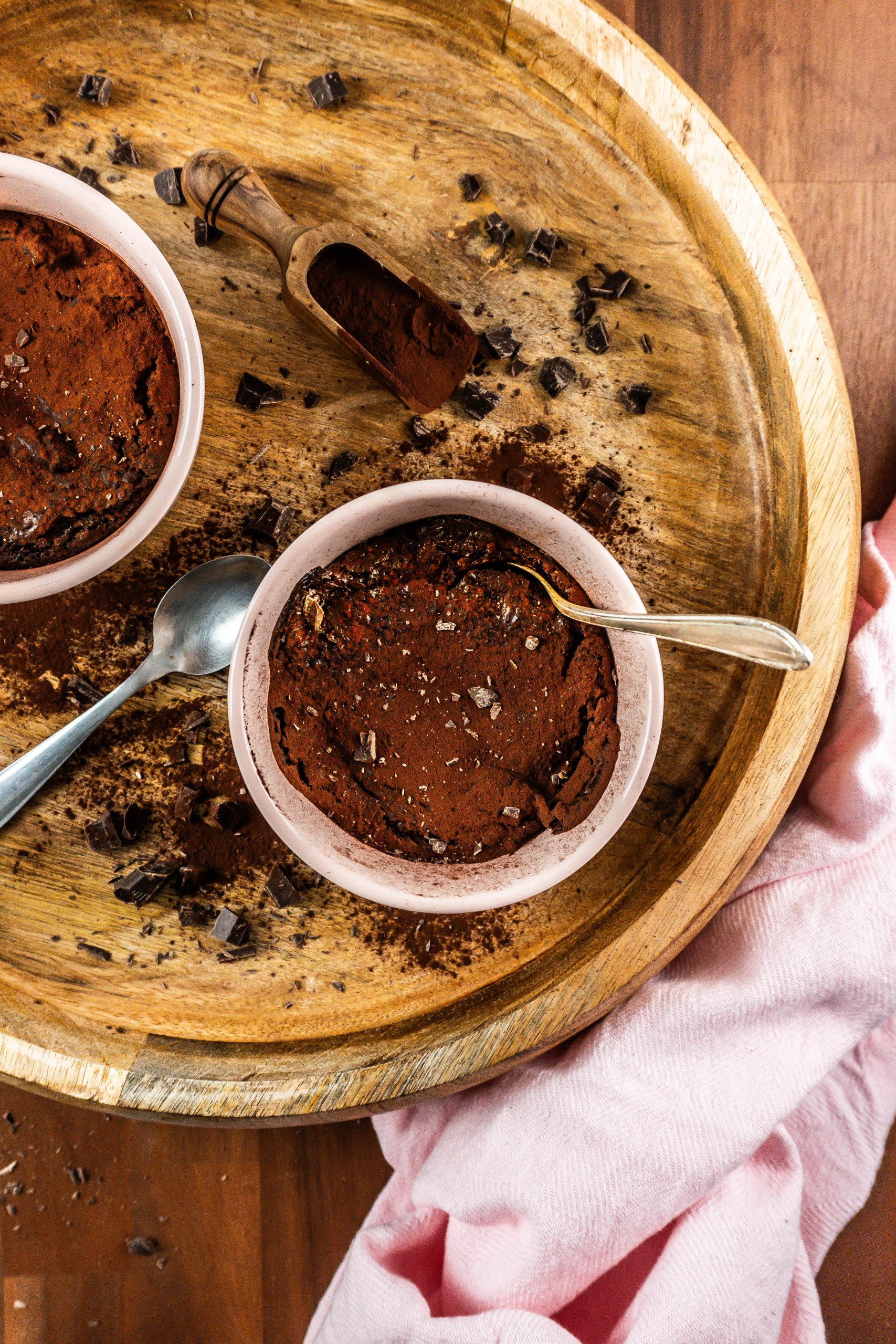 Gluten-free warm, fudgy mug brownie in in an oven-proof ramekin with a spoon tugged into it surrounded with chopped chocolate and cocoa powder